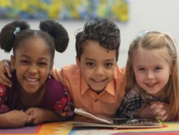 Three children smiling and lying on the floor with a book.