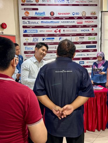 People interacting at a professional event with company logos in the background.