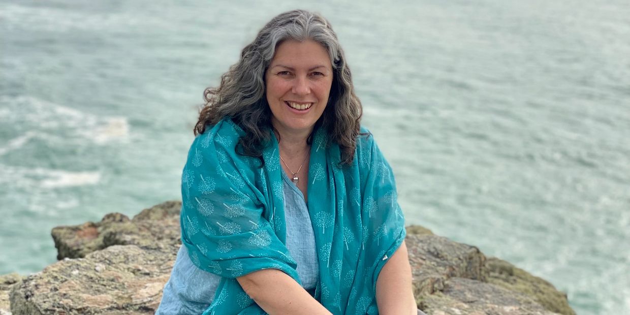 smiling and relaxed woman sitting on rock in front of sea 