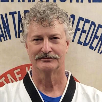Man with curly hair and mustache in a martial arts uniform.