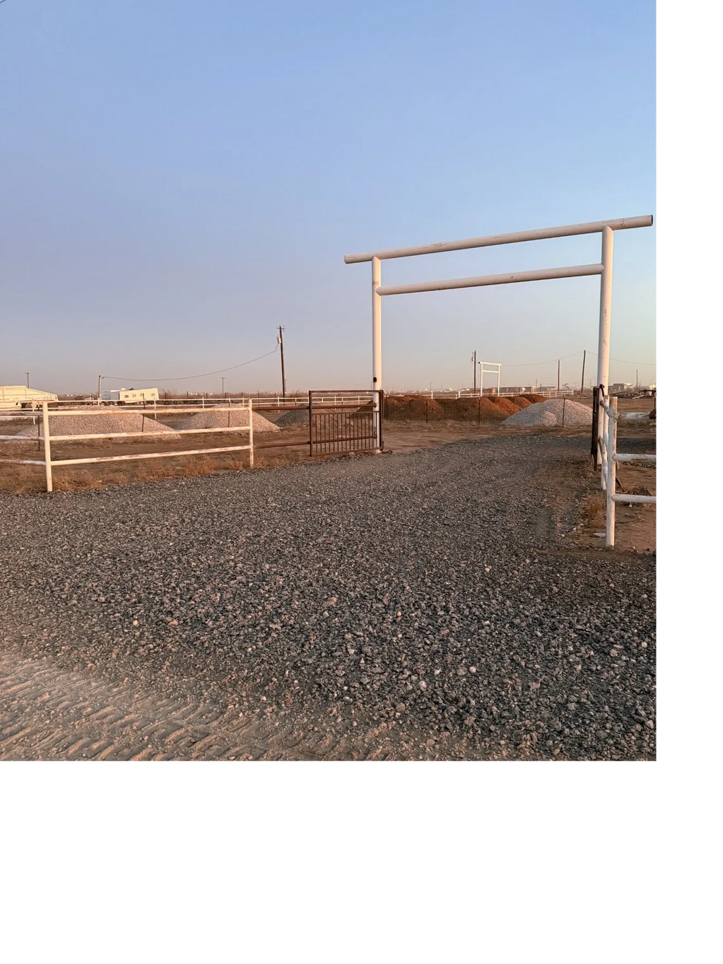 Gravel driveway entrance to a fenced rural property at sunset.
