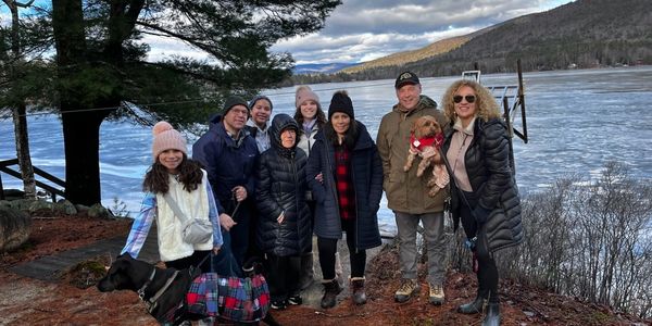 A family group with dogs posing by a frozen lake on a cloudy day.