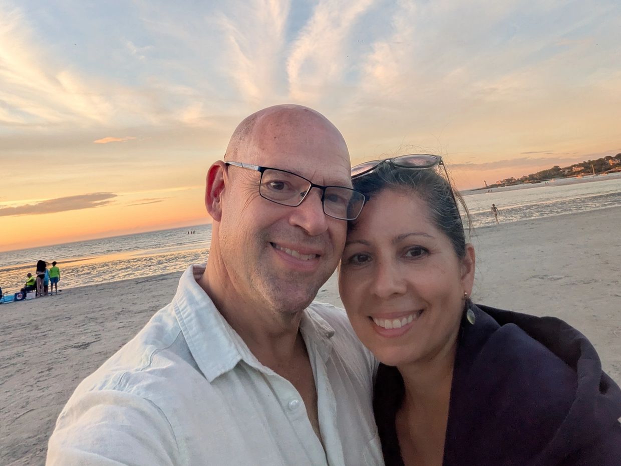Couple smiling together on a beach at sunset with beautiful cloud patterns.