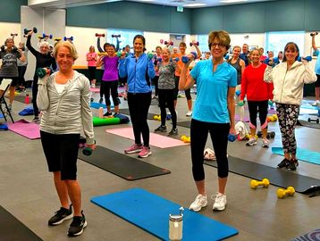 A group fitness class with women exercising using dumbbells.