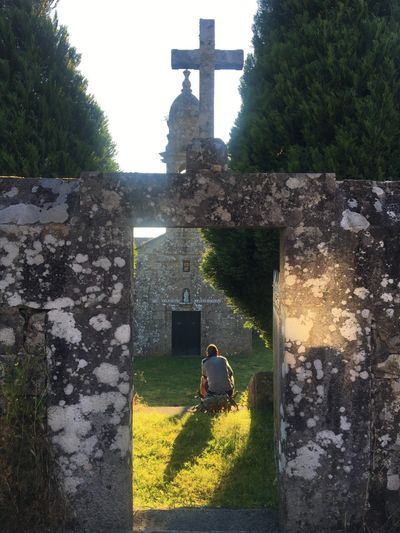 Person sitting near an old stone church with a cross.