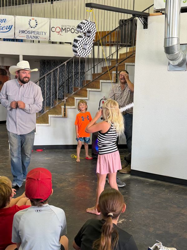 Children and adults play with a hanging piñata indoors.
