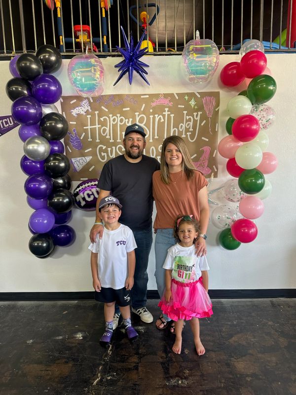 Family celebrating a birthday with colorful balloons and a handmade sign.