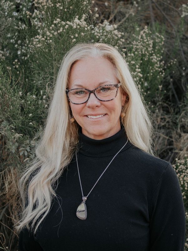 Smiling woman with long blonde hair wearing glasses and a black turtleneck.