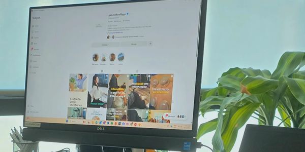 Person working at a desk with a Dell monitor and laptop showing social media content.