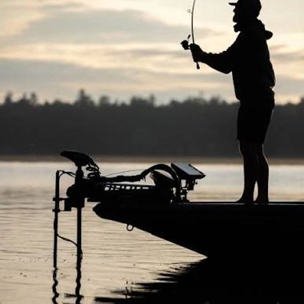 Silhouette of a person fishing from a boat at sunset.