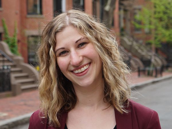 Smiling woman with curly blonde hair standing on a city street.