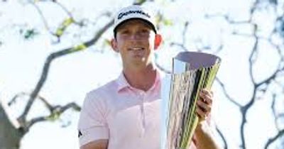 Golfer holding a large trophy outdoors, smiling.