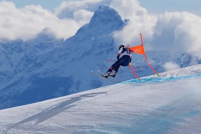 Skier in mid-air during a downhill race on a snowy mountain slope.