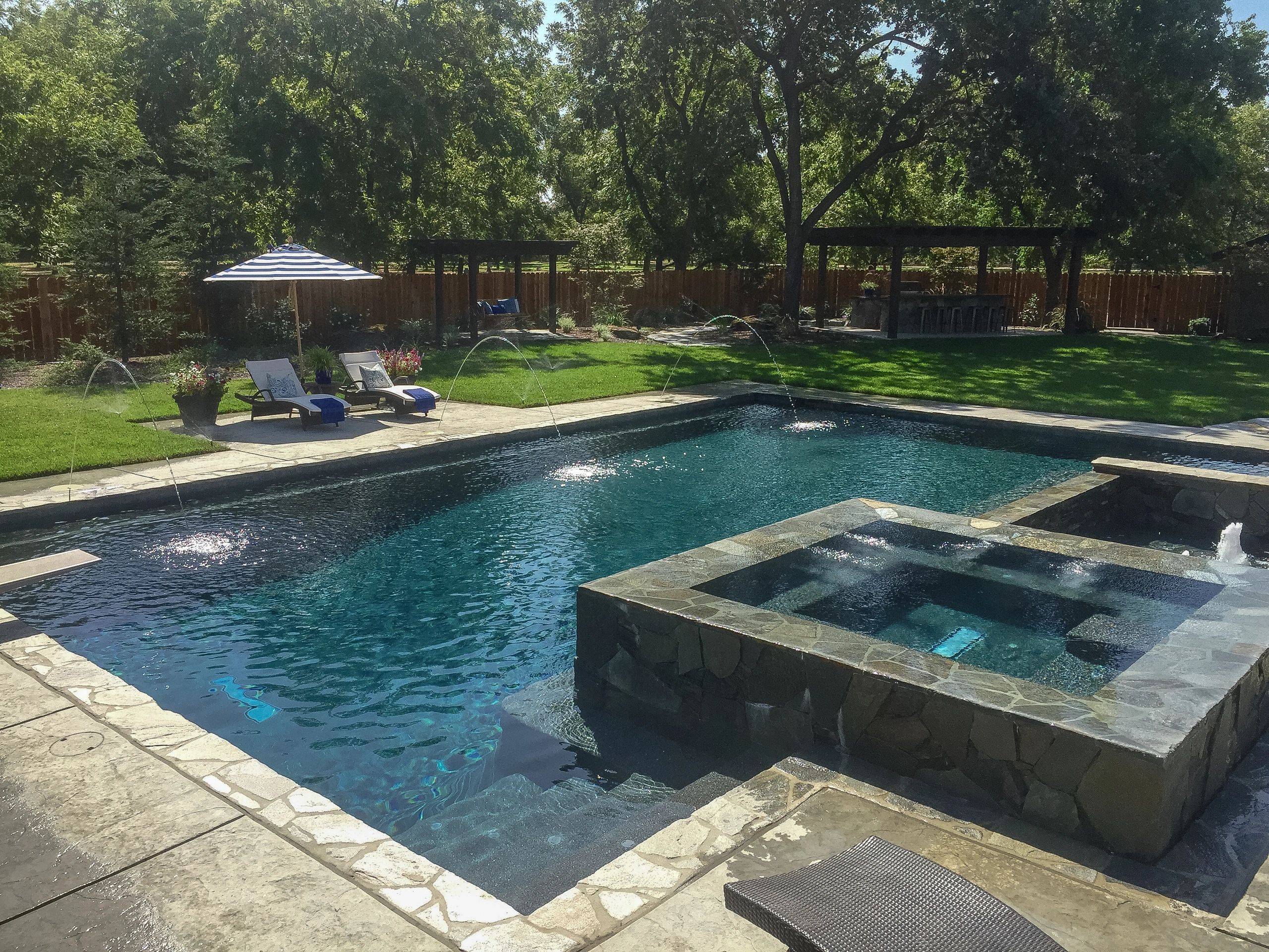 Elegant backyard pool with lounge chairs, water fountains, and a spa area surrounded by greenery.