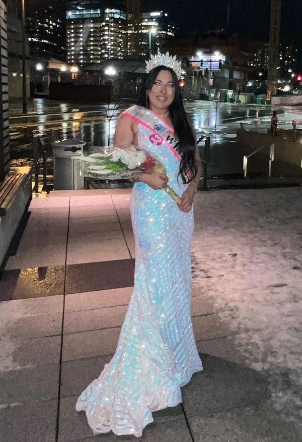 Woman in sparkling gown and crown holding flowers at night.