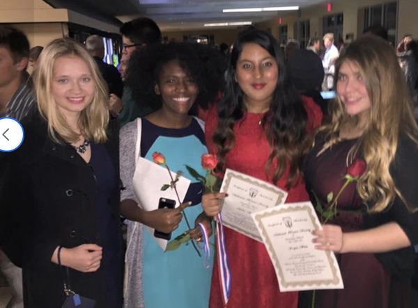 Four women smiling, holding roses and certificates at a celebration event.