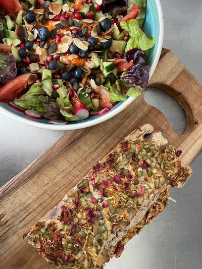 Fresh salad with blueberries and a seed-topped bread on a wooden board.