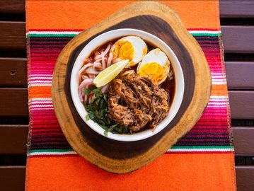 Bowl of savory noodle soup with shredded meat, boiled eggs, and lime wedge.
