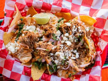 Plate of loaded nachos with shredded meat, cheese, and a lime wedge.