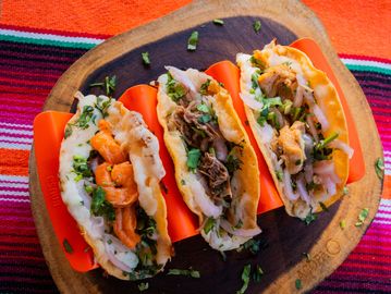 Three tacos filled with various meats and fresh herbs on a wooden board.