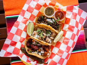 Three tacos with lime wedges and salsa on a checkered paper.