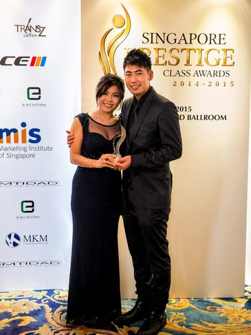 Two individuals posing with an award at the Singapore Prestige Class Awards 2014-2015.