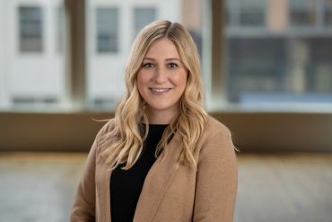 Professional woman with blonde hair in a brown blazer smiles confidently.