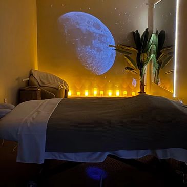 Cozy massage room with moon projection and candles.