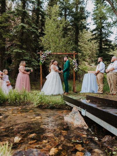 Outdoor wedding ceremony by a stream with bride, groom, and wedding party.
