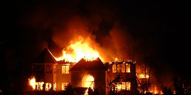 A large house engulfed in flames at night.
