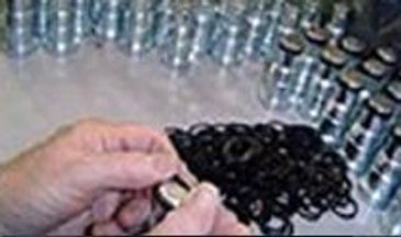 Hands inspecting a small black machined part among many others.