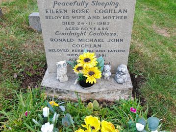 Gravestone with engraved names and dates, decorated with yellow flowers and small figurines.