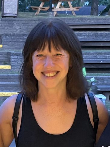 Smiling woman with dark hair in a black tank top outdoors.