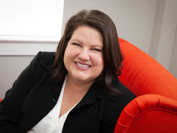 Smiling woman sitting on a bright orange couch in a cozy room.