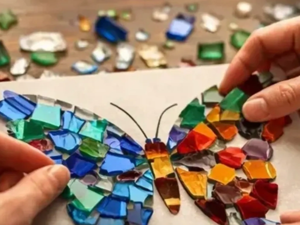 Hands assembling a colorful mosaic butterfly from glass pieces.