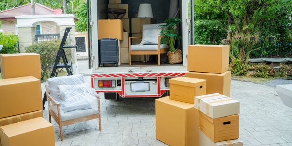 Moving boxes and furniture being loaded into a truck outside a house. Dependable moving packing services stress-free relocation.