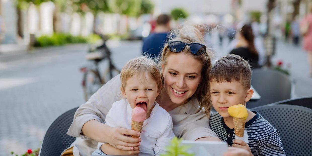 A mother and her two children enjoying ice cream outdoors on a sunny day.