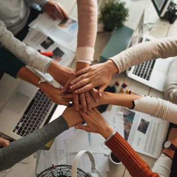 Team members join hands in a show of unity over a workspace.