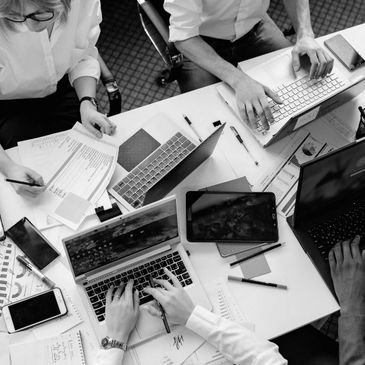 People working together at a desk with laptops, tablets, and documents.
