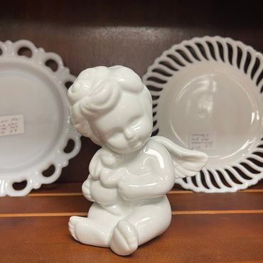 White ceramic cherub figurine sitting between decorative plates.
