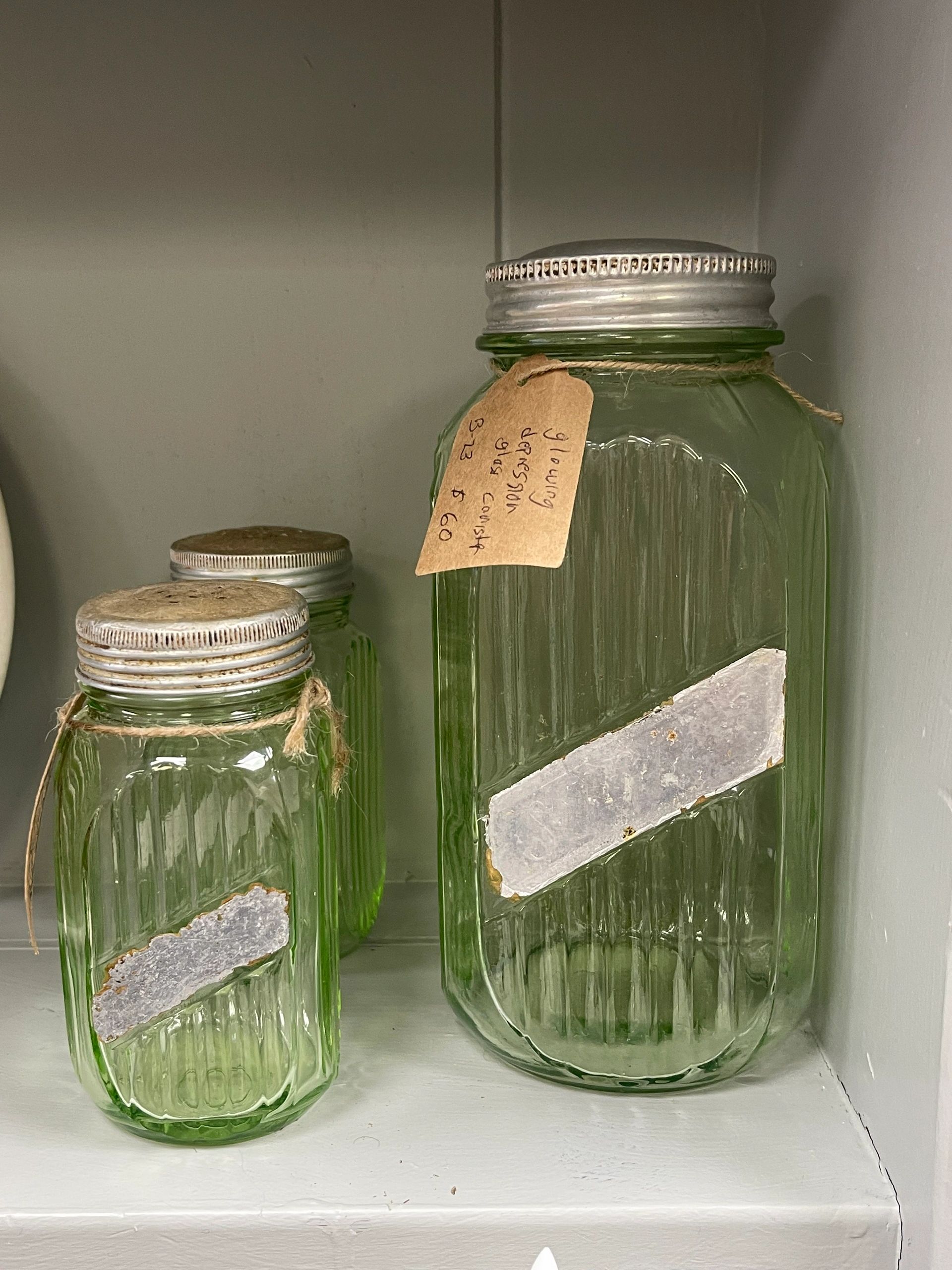 Three vintage green glass jars with metal lids on a shelf.