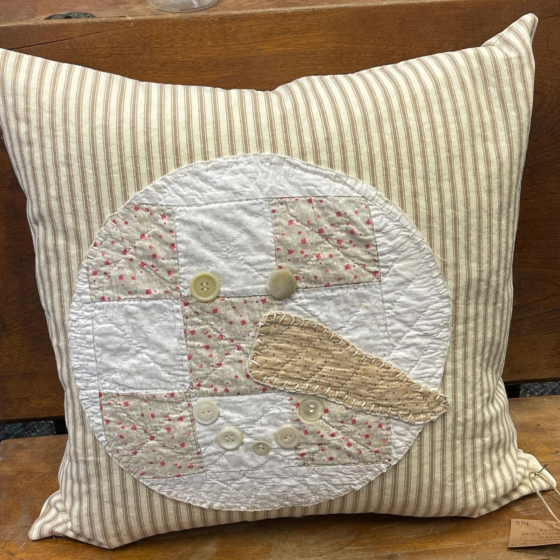 Striped pillow with a patchwork snowman face made of buttons and fabric.
