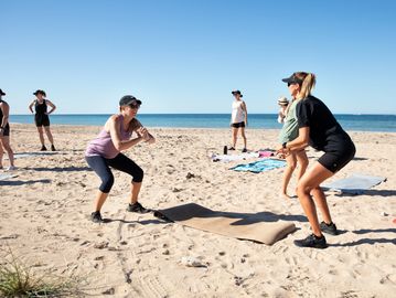 Group fitness class doing squats on a sunny beach.