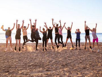 Group of women joyfully jumping on the beach at sunset.