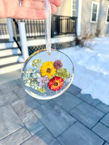 Hand holding a clear ornament with colorful dried flowers inside.