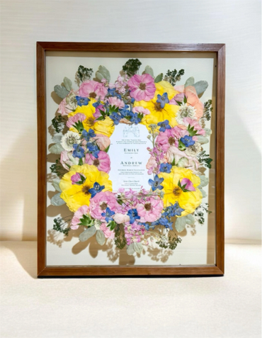 Framed floral wreath with a wedding invitation at the center.
