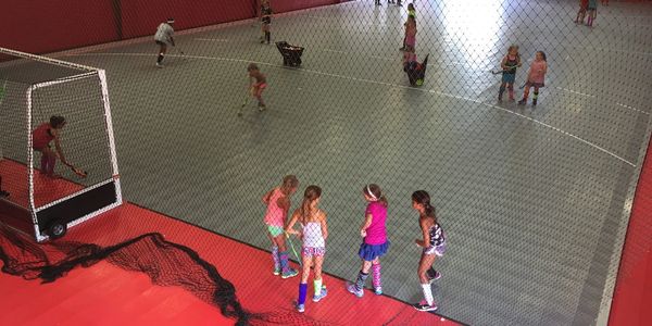 Children playing indoor field hockey on a court.