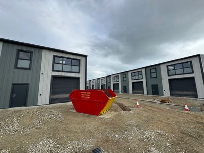 Red dumpster on a construction site with industrial buildings in the background.