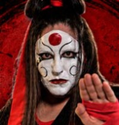 Person with white face paint and red accents holding up hand.