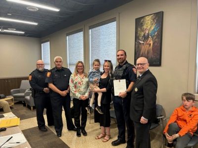 Group photo of police officers, family, and officials indoors.
